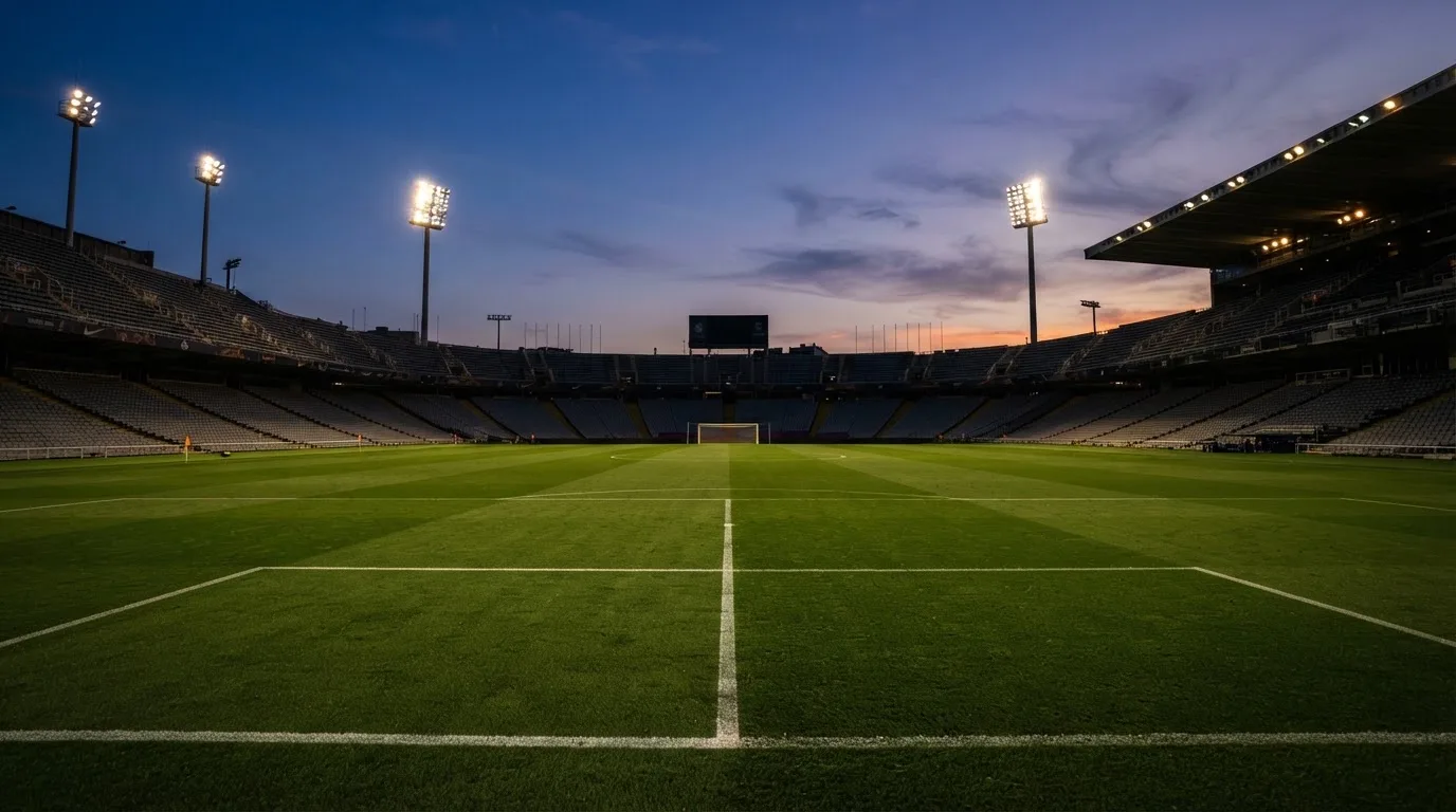 An empty football stadium with floodlight masts at dusk