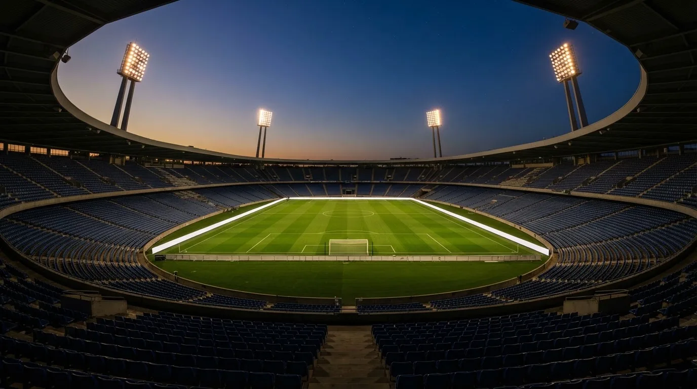 An empty football stadium with floodlight masts at dusk