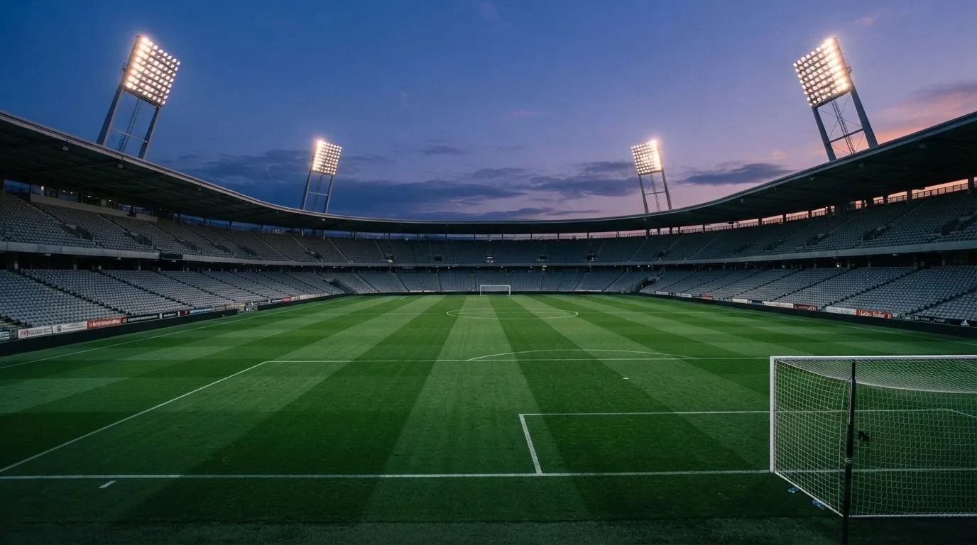 An empty football stadium with floodlight masts at dusk
