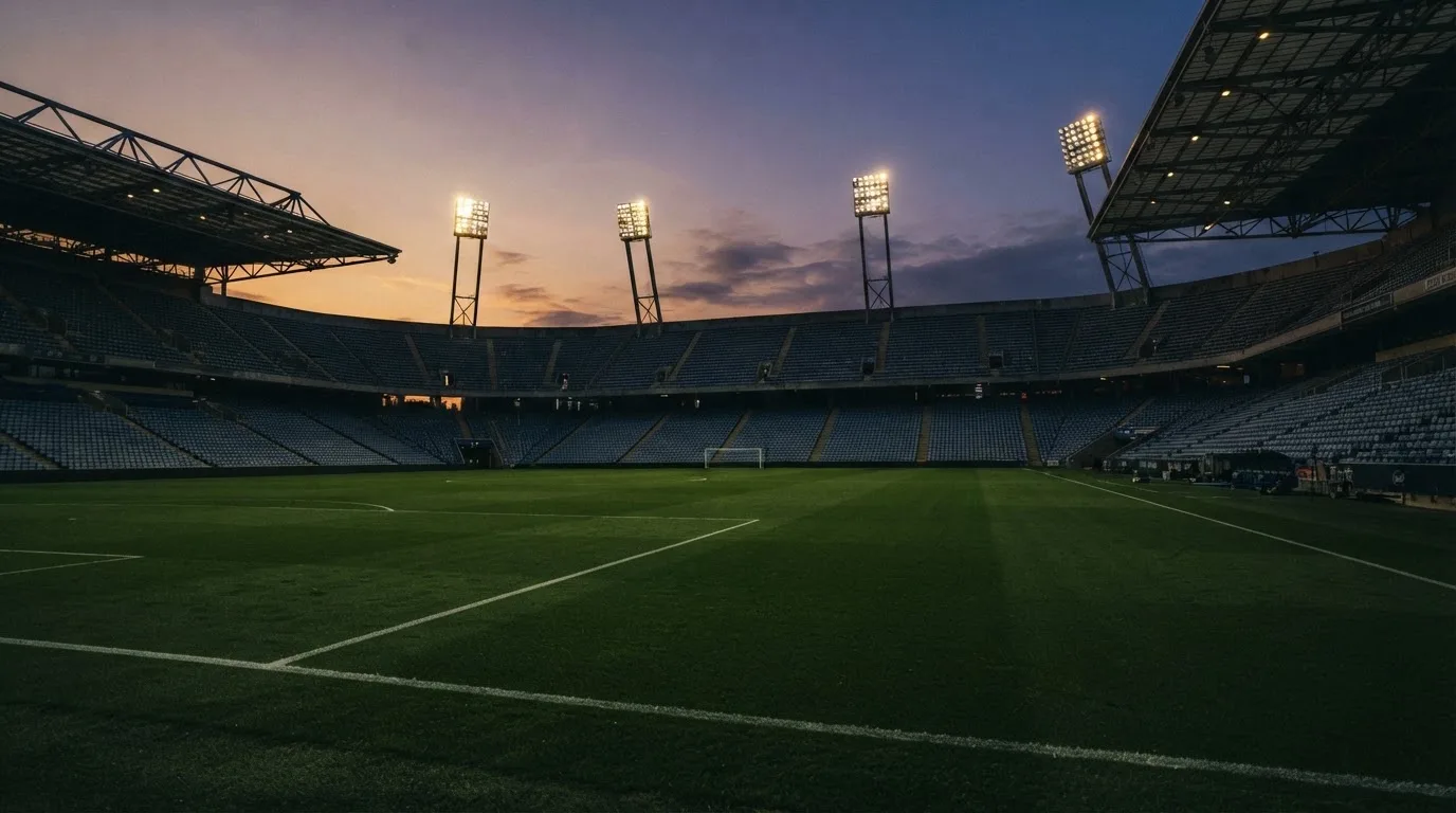 An empty football stadium with floodlight masts at dusk