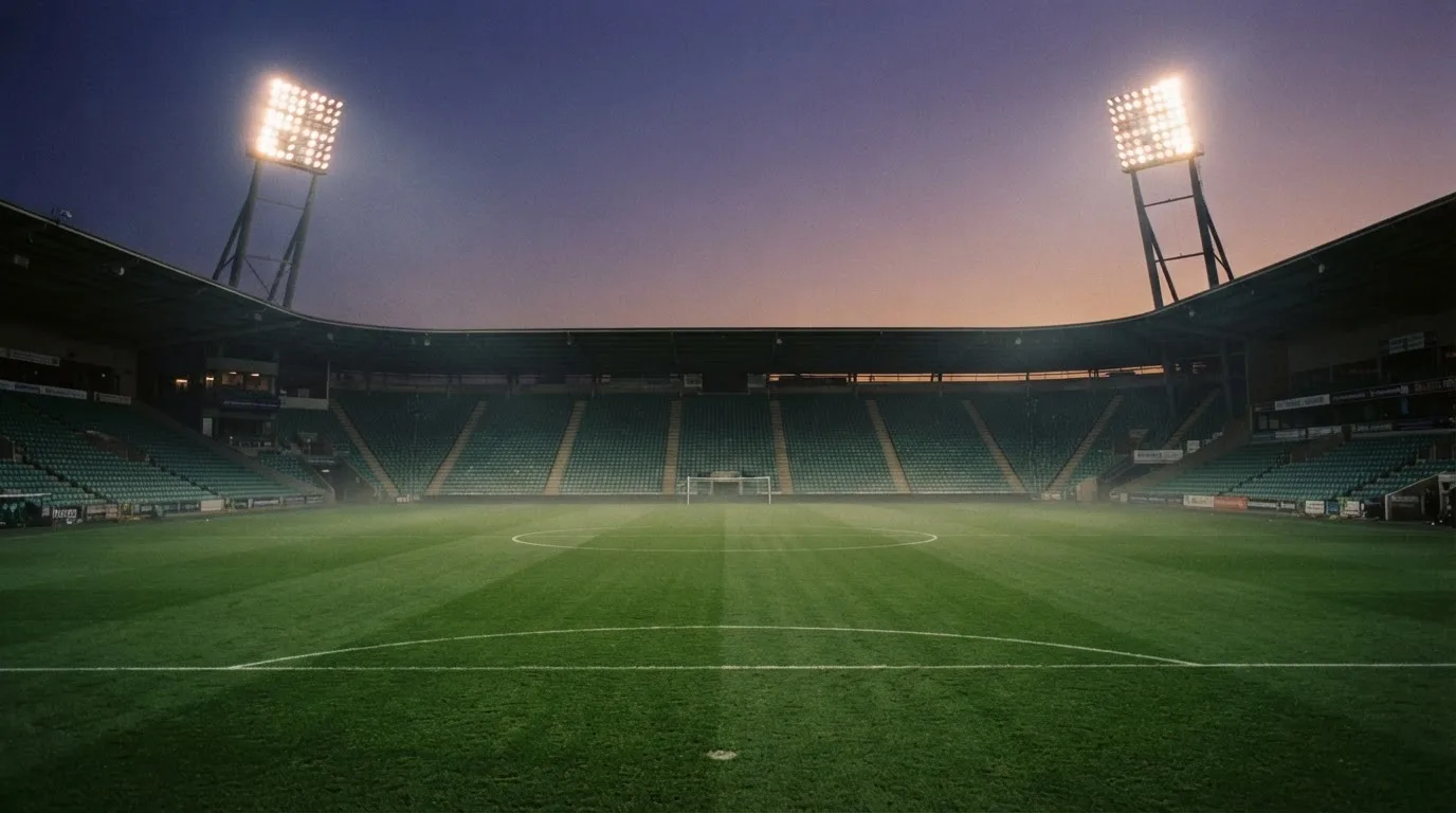 An empty football stadium with floodlight masts at dusk