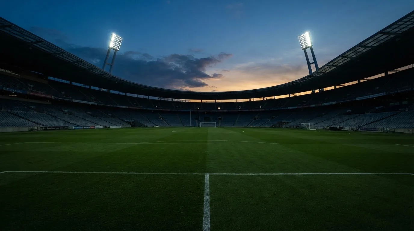 An empty football stadium with floodlight masts at dusk