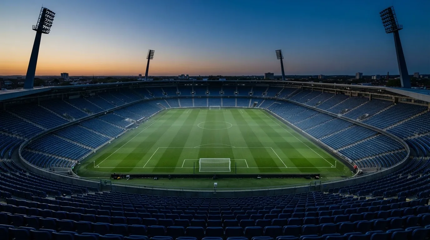 An empty football stadium with floodlight masts at dusk