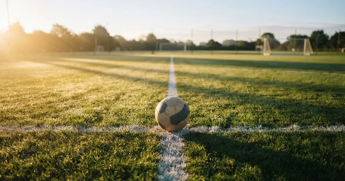 A ball on the centre spot of a grass pitch in morning light