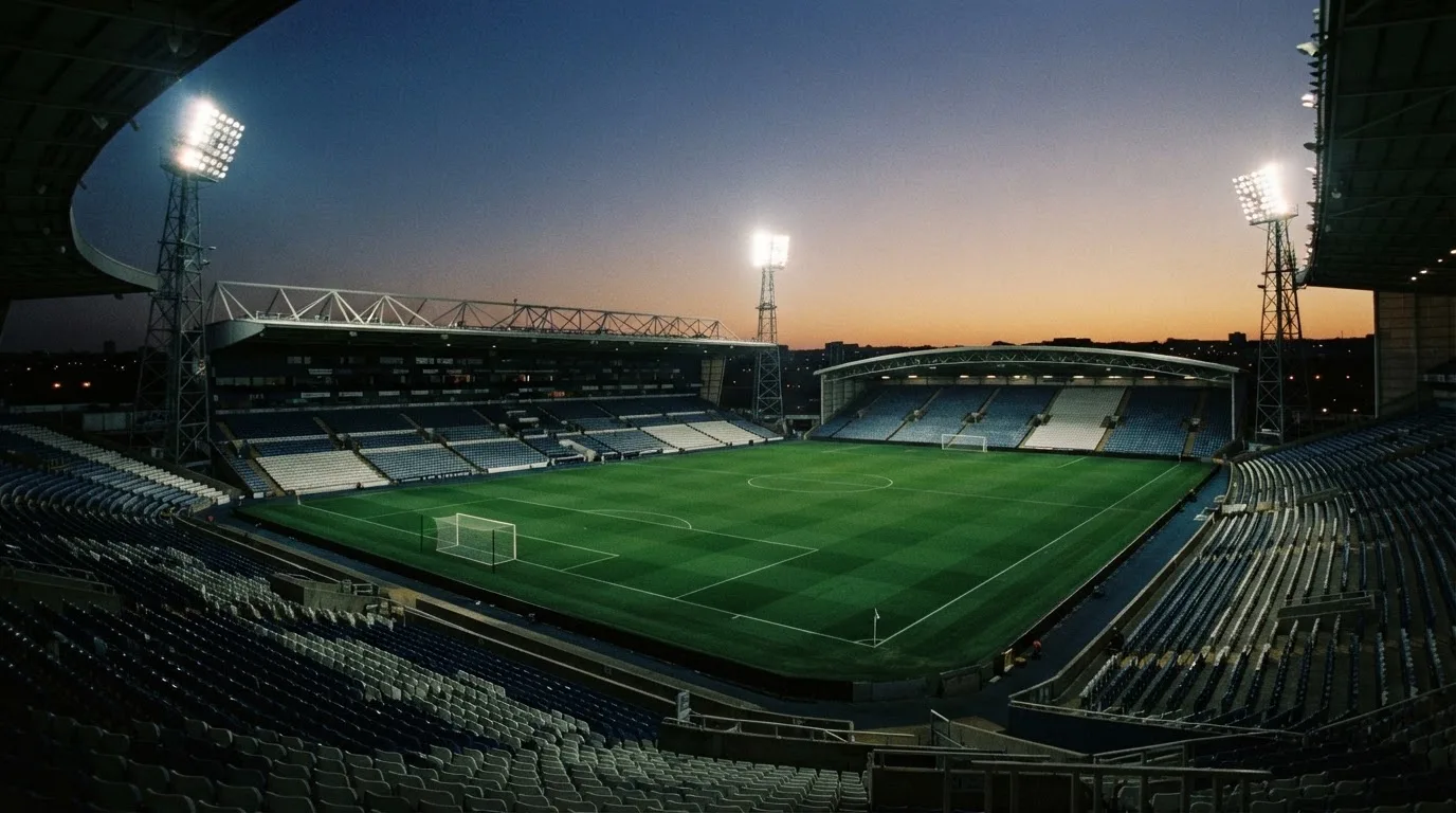 An empty football stadium with floodlight masts at dusk
