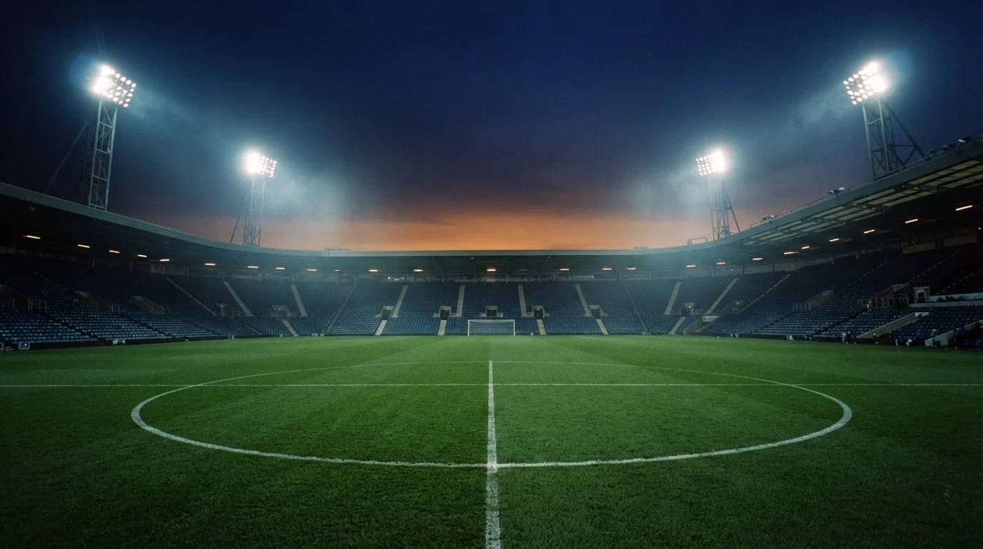 An empty football stadium with floodlight masts at dusk